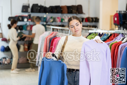 Young woman choosing sweatshirt in store