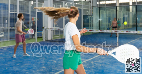 Teenage girl serving ball while playing padel in court