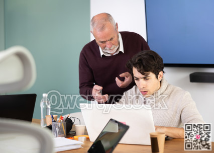 Mature male manager helping to guy during working at laptop in office