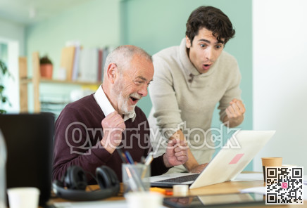Happy young and elderly men colleagues cheering at successful result on laptop