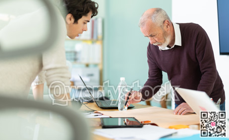 Two men are bent over drawing, reviewing and discussing development of construction.