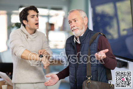 Young man scolding elderly male colleague for being late to office