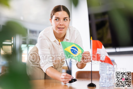 Young female assistant putting up swiss and brazilian flags on table for international negotiations