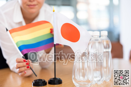 Rainbow flag and flag of Japan in female hands on negotiating table