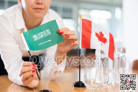 Young woman putting flags of Saudi Arabia and Canada on table in office
