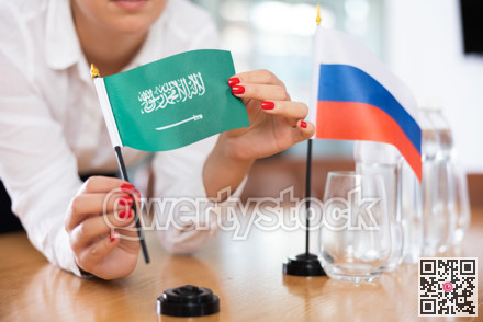 Flags of Saudi Arabia and Russia stand on negotiating table in office