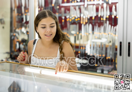 Young woman making choice against the background of stand with knifes