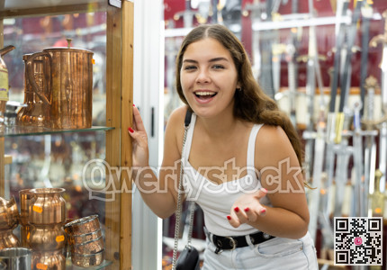 Interested young woman viewing copper utensil placed on display case