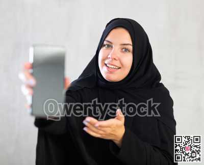 Smiling young woman dressed in traditional islamic clothes displaying brand new smartphone
