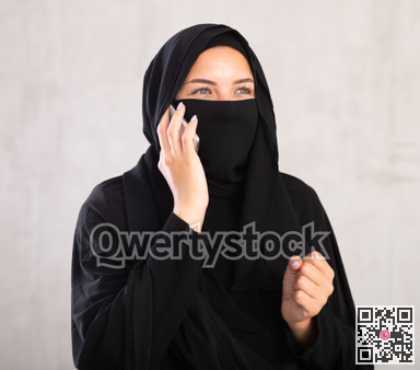 Young woman dressed in traditional islamic clothes with her face covered having phone conversation