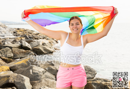 Portrait of a playful girl holding an LGBT flag in her hands on the beach on sunny day