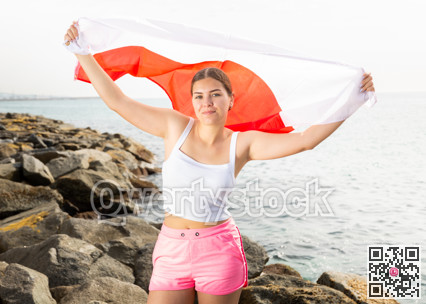 Young woman on coast posing with flag of Poland