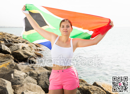 Young woman on coast posing with flag of South Africa