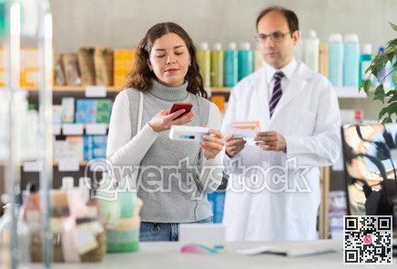 Male pharmacist in medical uniform helps customer in casual clothes find baby formula from photo on Internet