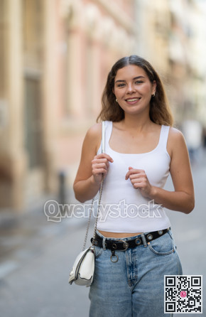 Cheerful girl walking at the street among architecture with bag