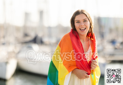 Happy girl waving LGBT flag against seaport and yachts