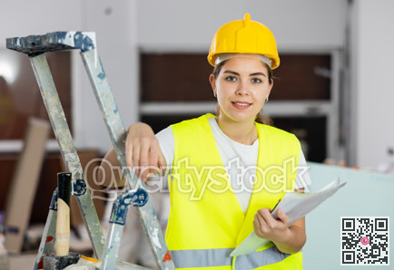 Woman foreman in a protective helmet and yellow vest checks the completed construction work on drawing