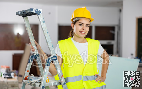 Portrait of female foreman in protective yellow vest and hard hat in room being renovated