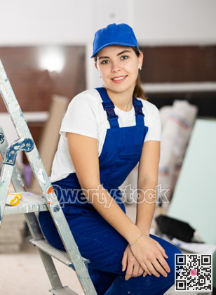 Positive builder woman in blue overalls next to stepladder