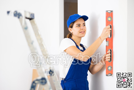 Woman builder using building level measures the vertical of wall