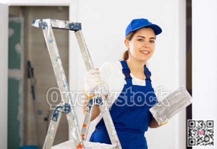 Portrait of young woman builder with trowel standing in apartment