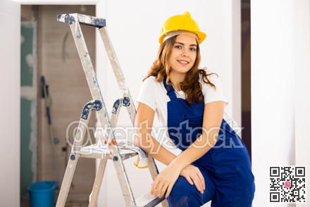 Portrait of contented young female builder in blue overalls during the repair of cottage