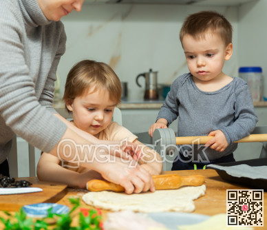 Mother and two young boys making pizza together in home kitchen