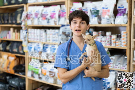Positive young veterinarian standing in veterinary clinic with chihuahua in hands