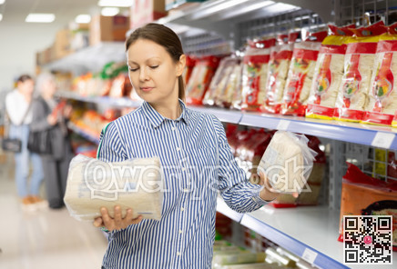 Interested woman reading label on packages of Asian noodles in supermarket