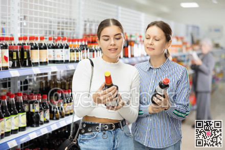 Girl customer with female friend is thinking about buying spicy and unusual soy sauce.