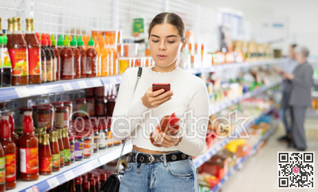 Young girl scanning barcode with smartphone on bottle of sauce in store