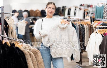 Young girl choosing short fur coat in clothing shop
