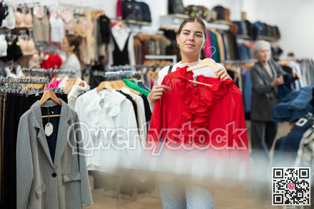 Young girl choosing red blouse in clothing store
