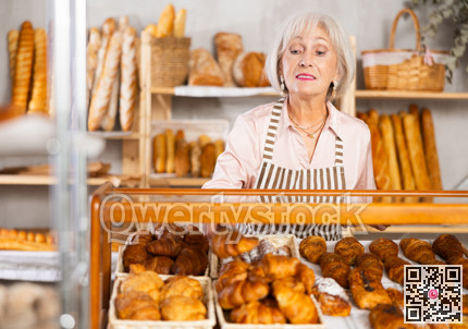 Elderly bakery saleswoman places fresh croissants on display