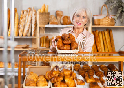 Elderly bakery saleswoman places fresh croissants on display