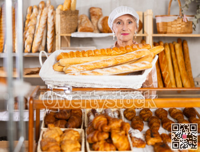 Senior female baker worker sells baguette, shows many products