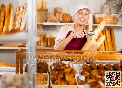 Elderly female bakery salesperson offers to buy bread, baguettes and croissants