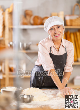 Mature woman chef stands at his work bench, kneading and shaping dough to make bread, croissants and baguettes