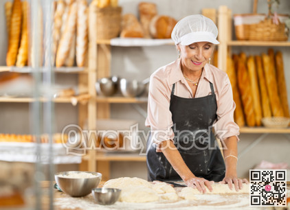 Elderly female chef skillfully kneads dough to bake delicious bread and croissants