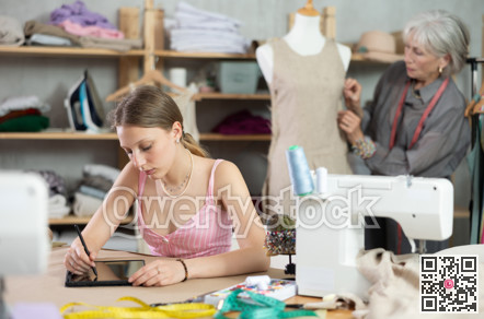 Female tailor drawing design on tablet with mature female worker in background