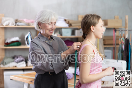 Elderly seamstress takes body measurements from young woman