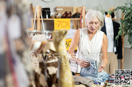 Elderly woman chooses fashionable jeans in clothing store for summer season