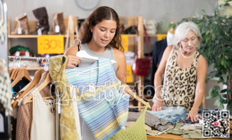 Positive young woman choosing something for summer in clothing store
