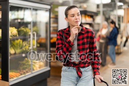 Visiting store woman is looking at something on shelf of showcase, client buy goods