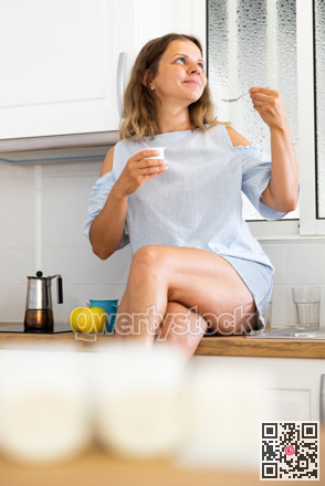 Young woman eating tasty yogurt in kitchen