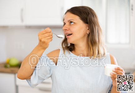 Young woman eating tasty yogurt in kitchen