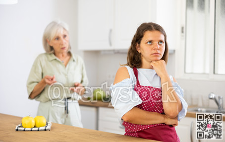 Senior woman scolding her adult daughter cooking breakfast in modern kitchen