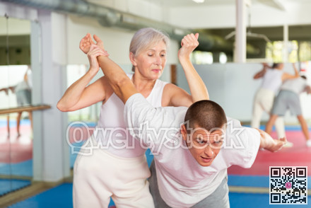 Elderly woman performing elbow strike and wristlock to man in self defense training