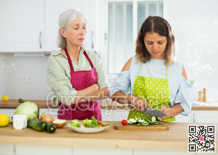 Old woman in apron observing her daughter cooking salad