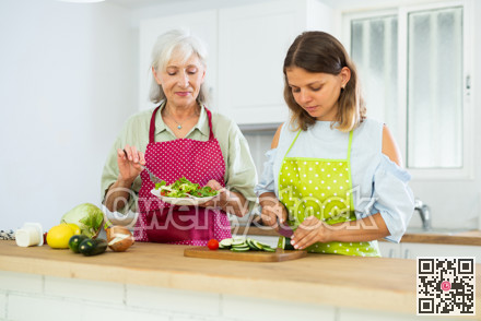 Senior woman and her adult daughter cooking salad together